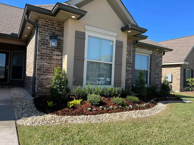 Tan brick home with a rock border along the front garden bed.