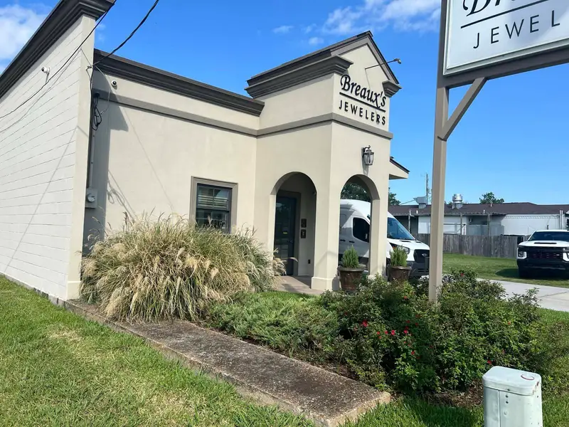Overgrown grass and shrubs in front of Breaux's Jewelers.
