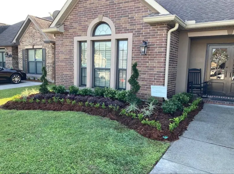 Shrubs and flowers in a mulched bed along a brick home.