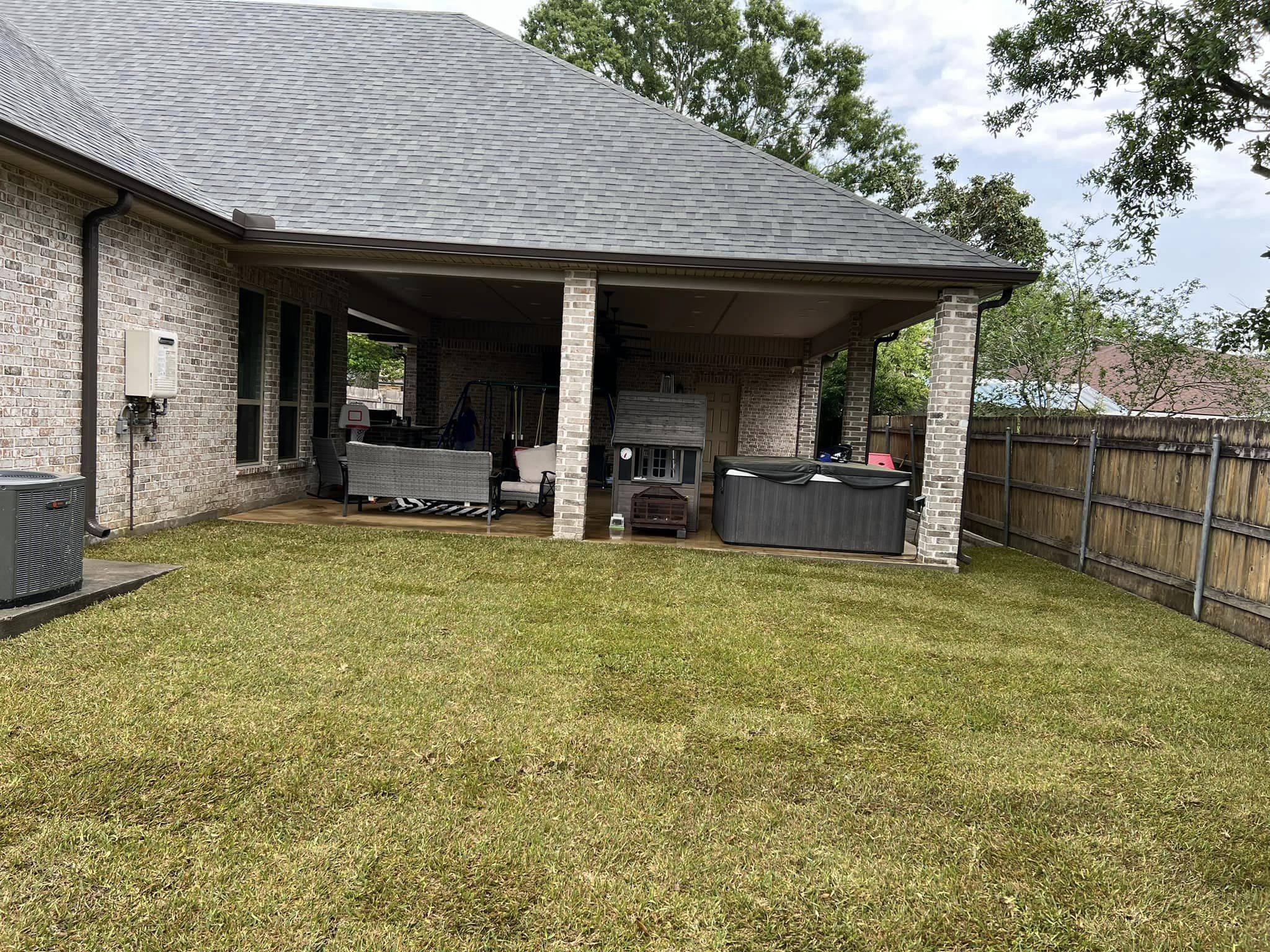 Newly installed sod creating a lush green lawn in a residential backyard with a covered patio and wooden fence, serviced by Southern Grounds, LLC.