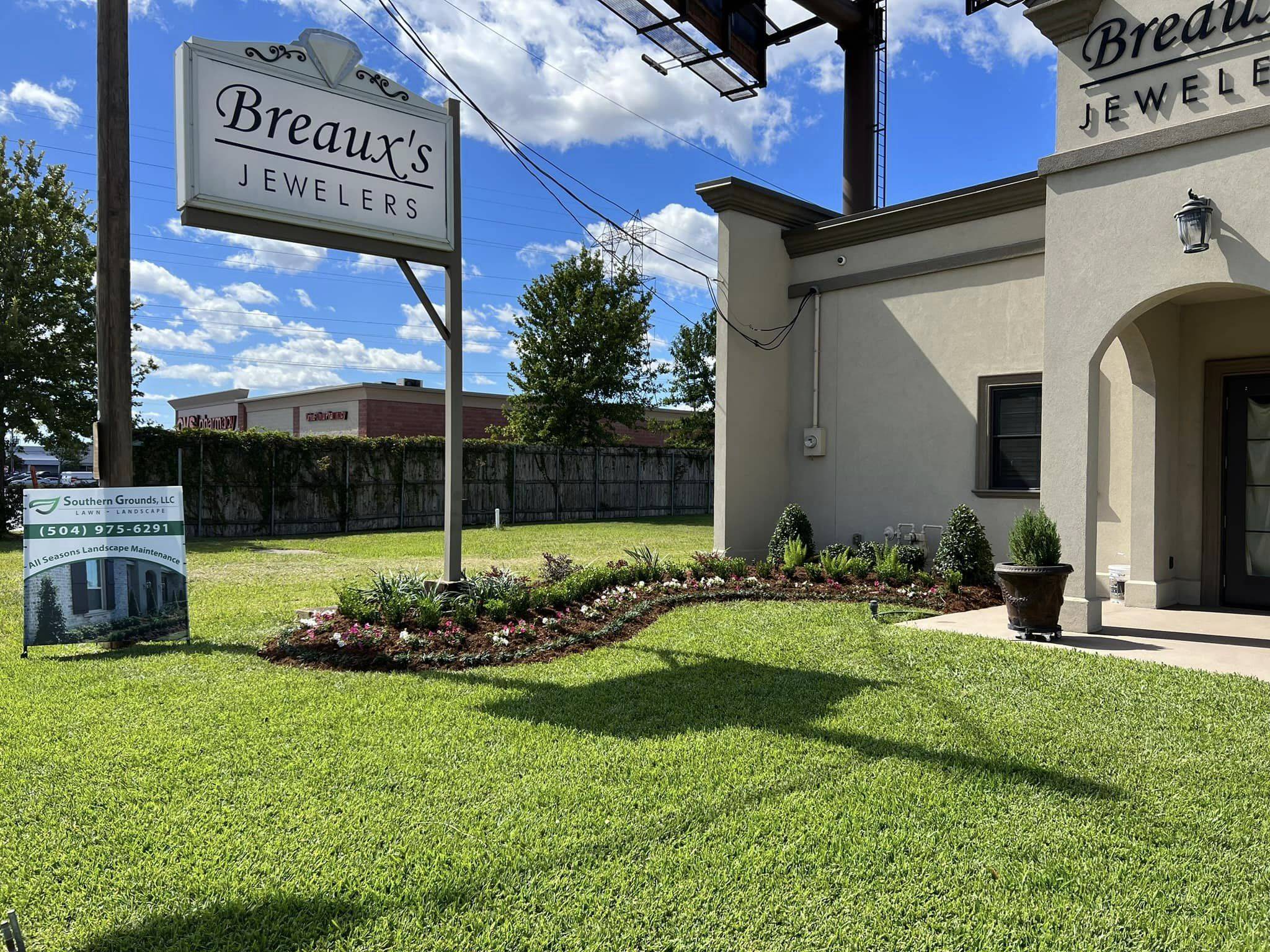 Elegantly redesigned garden with vibrant flowers and sculpted shrubs enhancing the commercial space near the Breaux's Jewelers signpost.